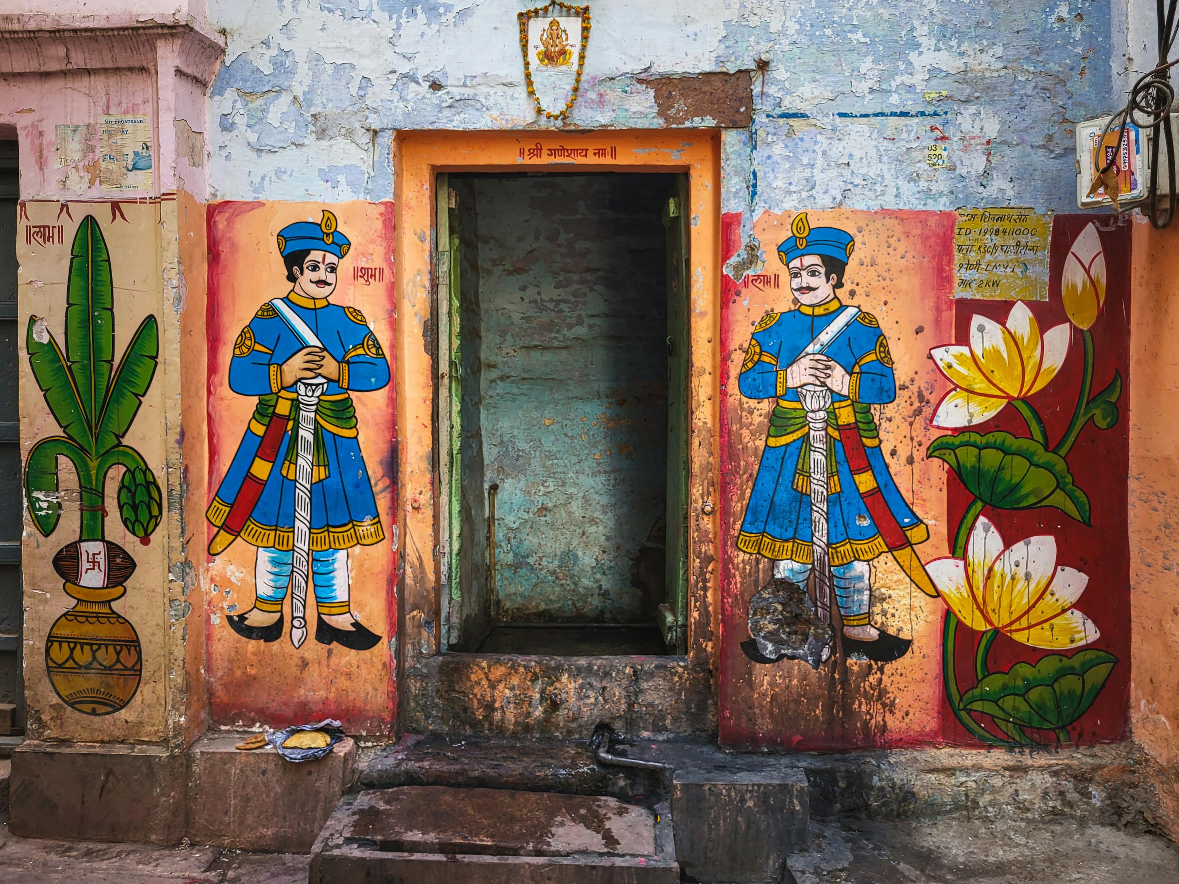 Colorful traditional Indian murals of guards and lotus flowers framing a weathered doorway, inspiring eclectic global summer decor trends.